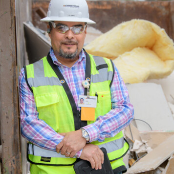 Construction worker in PPE standing in front of a dumpster