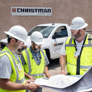 Three construction workers in PPE in front of a CFS truck looking at a blueprint
